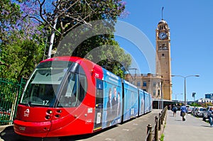 Red light rail running on the track at Pitt St. with Iconic central railway station clock tower at the background.